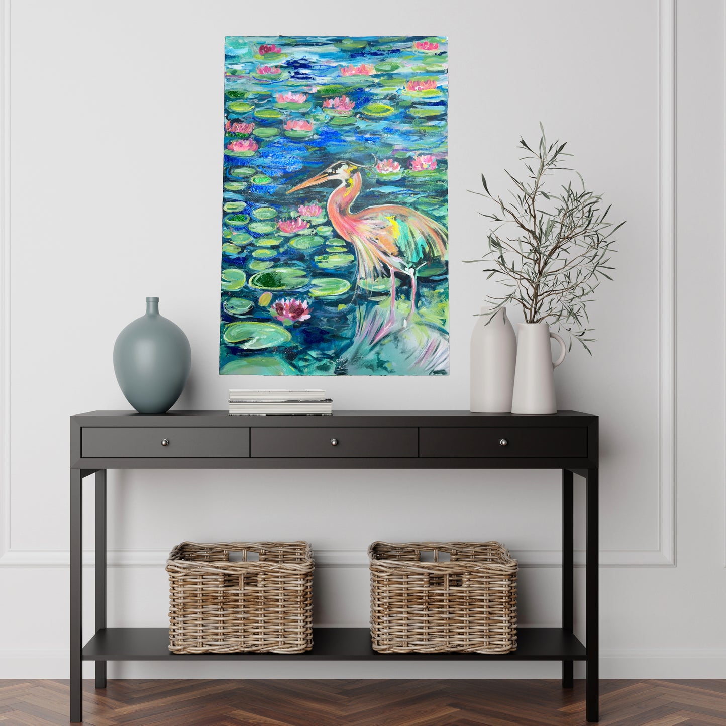 Mixed media painting titled 'Sparkling Blue Crane in Lily Pond' by Natalie Zoghby displayed on a white wall above a black console table with decorative vases. The vibrant artwork, featuring a blue crane surrounded by lily pads and flowers, adds a touch of color and nature to the modern, minimalist interior space.