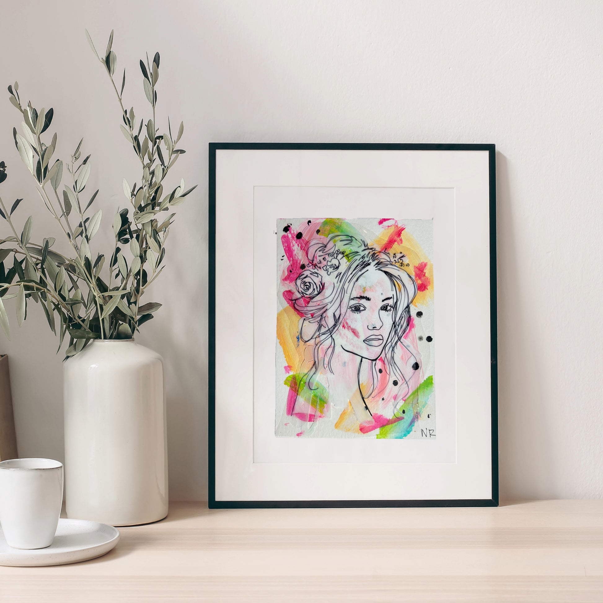 5x7 inch framed painting by Natalie Russo, featuring a delicate line drawing of a goddess with bright colorful acrylic accents, displayed on a minimalist counter.