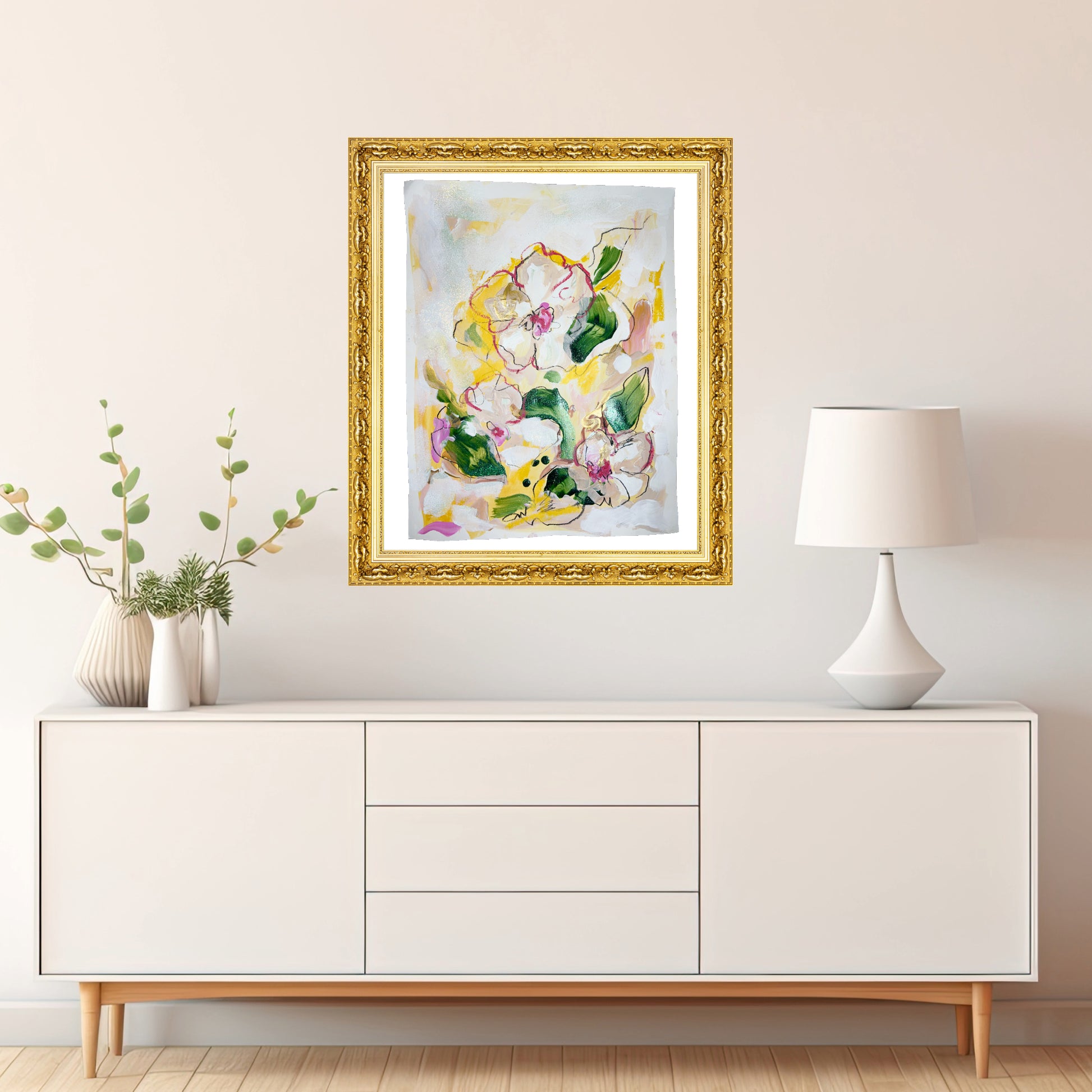 Original mixed media painting titled 'Golden Floral Harmony' by Natalie Russo, displayed in a gold frame above a modern white sideboard with a lamp and decorative vase. The artwork features a vibrant floral bouquet with shimmering gold accents, adding a warm and elegant touch to the interior.