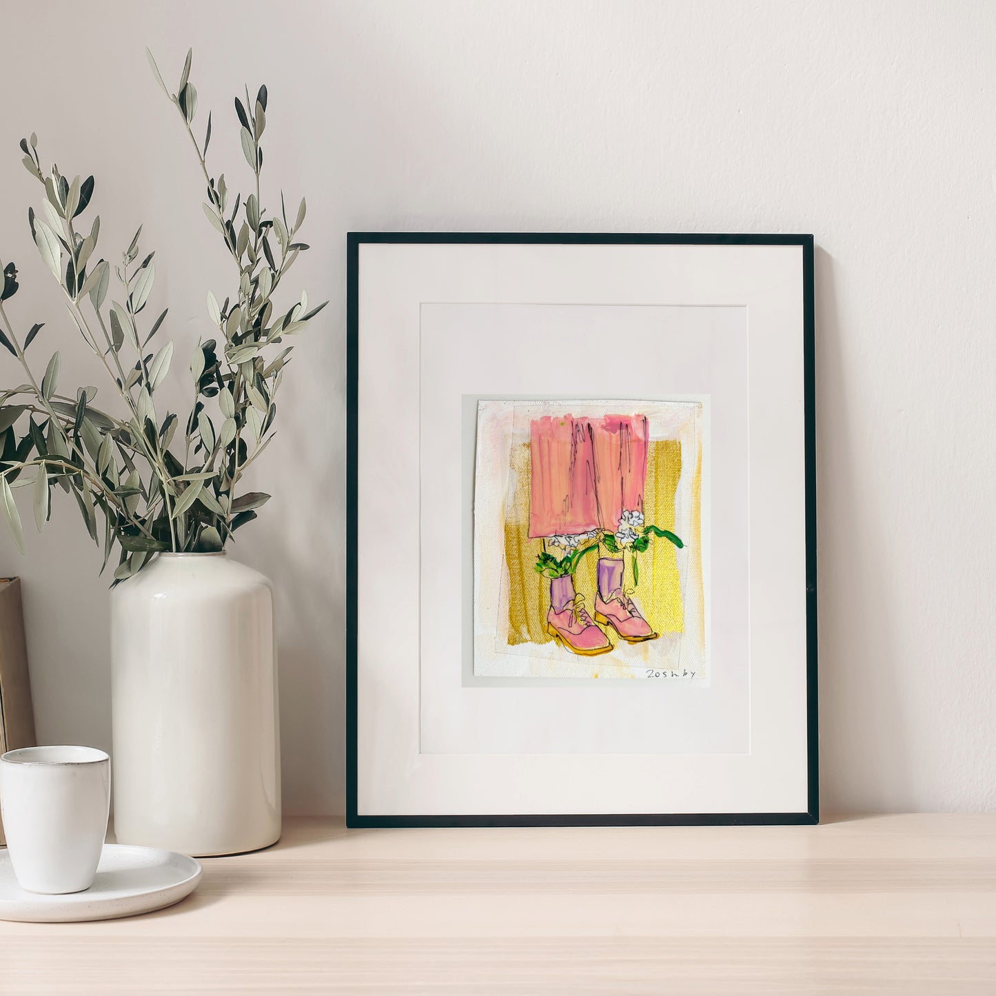 5x6 inch painting of pink shoes with flowers by Natalie Russo, framed and displayed on a tabletop next to a white vase. The acrylic painting features a gold background and whimsical design.